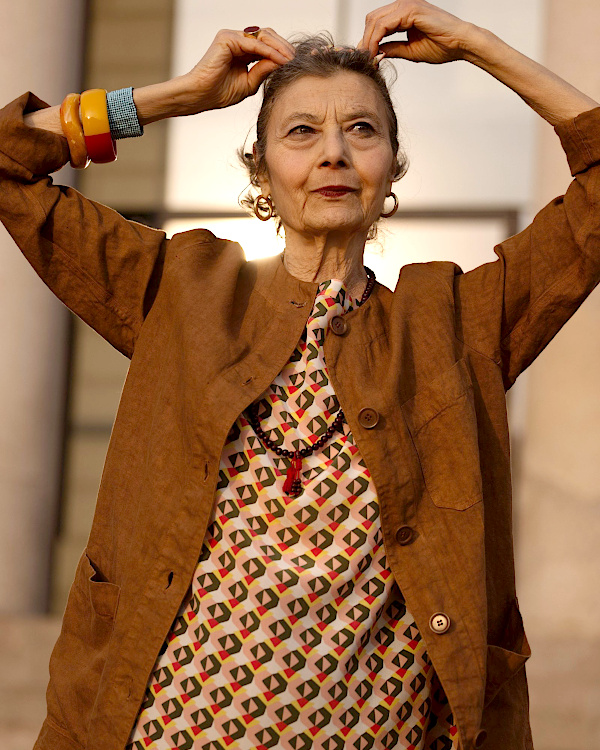 Femme de 70 ans avec sac structuré, foulard léger et chaussures sobres dans une tenue printanière élégante