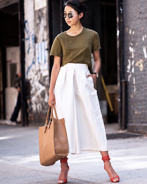 Femme portant une jupe-culotte blanche avec un tee-shirt kaki, un sac camel et des sandales rouges