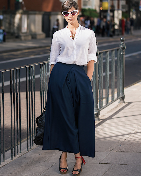 Femme en jupe-culotte bleu marine portée avec une chemise blanche fluide et des lunettes blanches