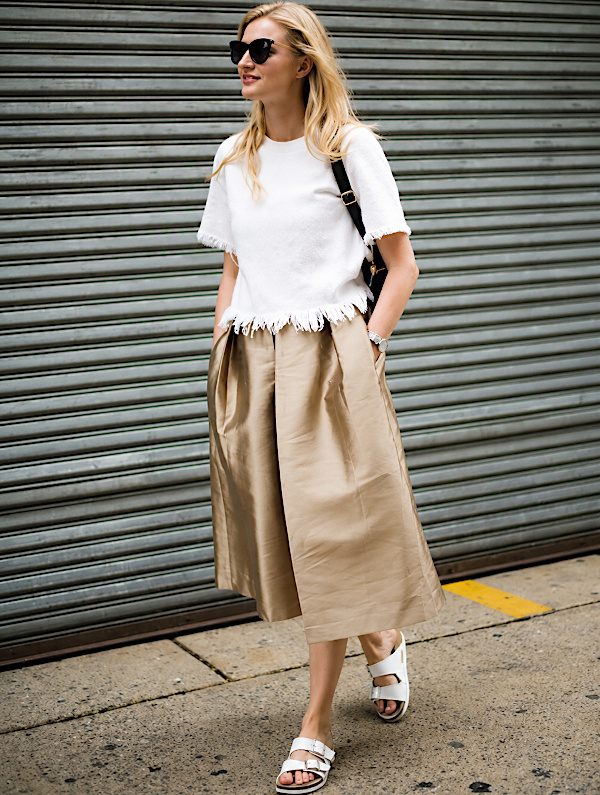 Femme blonde portant une jupe-culotte beige avec un haut blanc à franges et des sandales plates