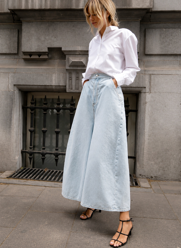 Femme portant une jupe-culotte longue en denim clair avec une chemise blanche et des sandales noires