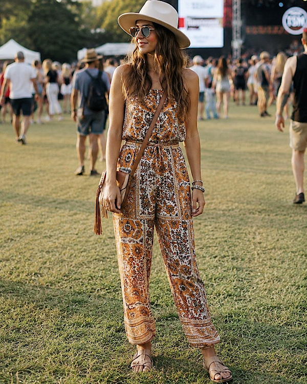 Femme en combinaison imprimée, chapeau et sandales plates dans un festival en plein air